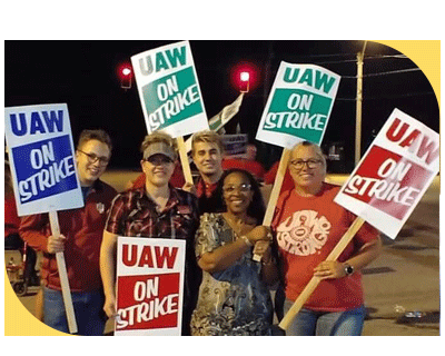 A group of people standing on a union picket line holding signs that read "UAW ON STRIKE"