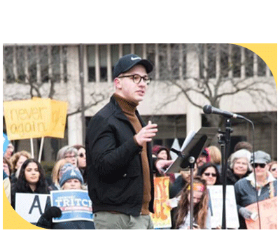 Brandon Blumenherst speaking to a crowd of people holding signs at a gun violence prevention rally